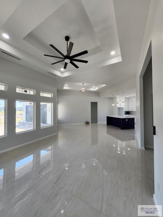 unfurnished living room with a raised ceiling, baseboards, and ceiling fan with notable chandelier