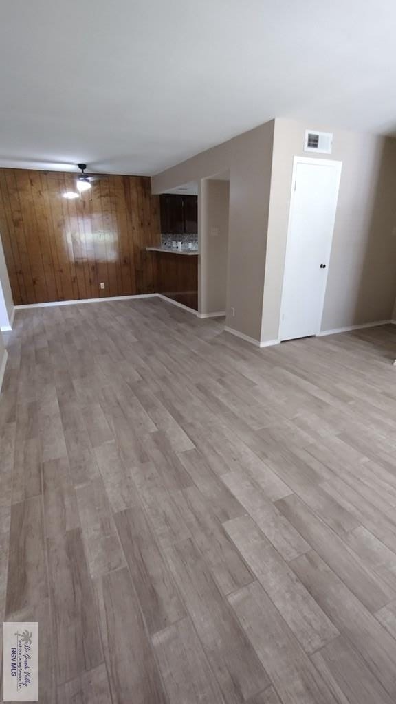 unfurnished living room with wooden walls, ceiling fan, and light wood-type flooring