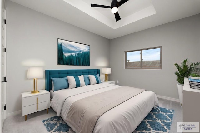 carpeted bedroom with a raised ceiling and ceiling fan