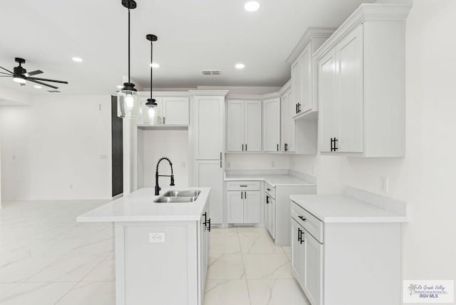 kitchen with ceiling fan, sink, decorative light fixtures, white cabinets, and an island with sink