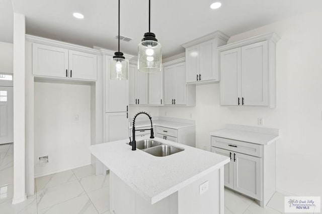 kitchen featuring pendant lighting, white cabinetry, a kitchen island with sink, and sink