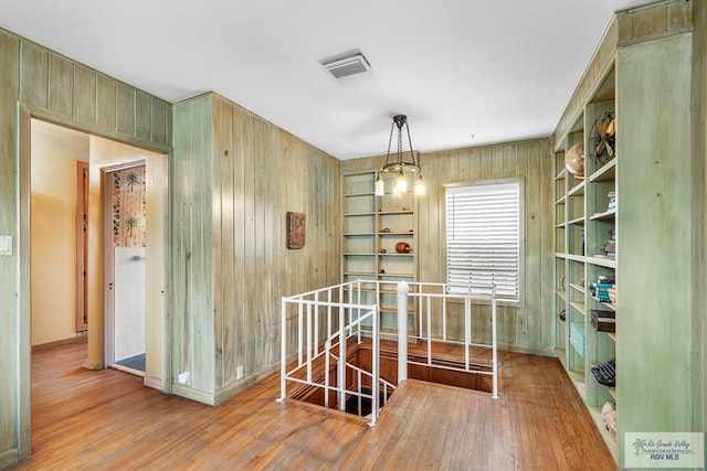 hallway featuring an inviting chandelier, hardwood / wood-style flooring, and wooden walls