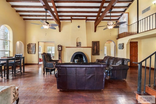 living room featuring dark wood-type flooring, ceiling fan, a towering ceiling, and beamed ceiling