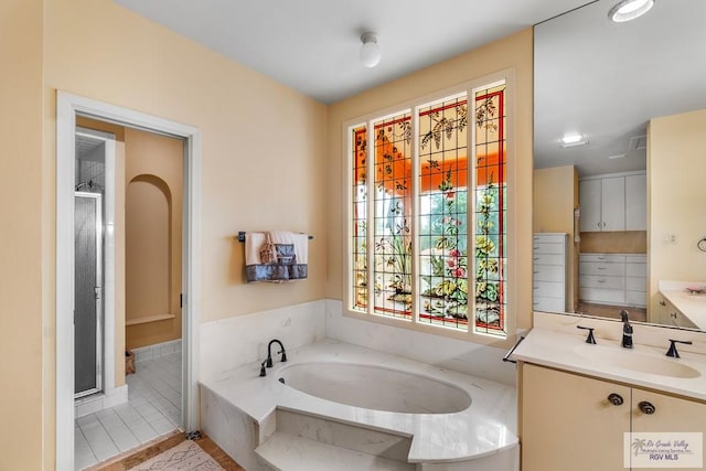 bathroom with tile patterned flooring, vanity, and a relaxing tiled tub