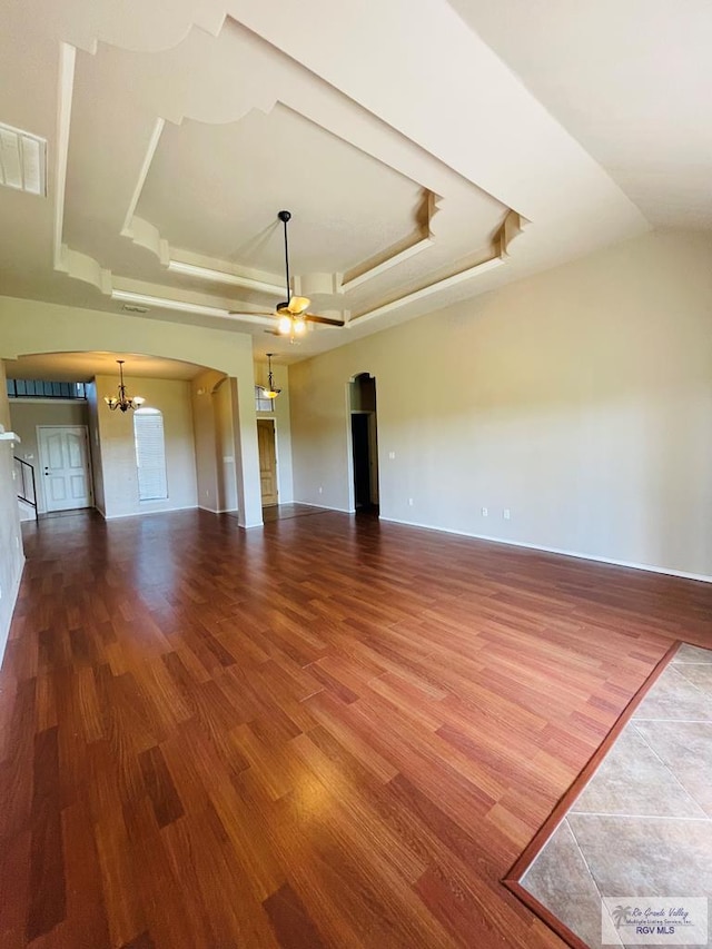 unfurnished living room with a raised ceiling, ceiling fan with notable chandelier, and hardwood / wood-style flooring