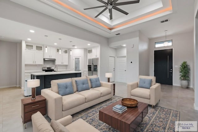 living room featuring ceiling fan, a raised ceiling, and sink