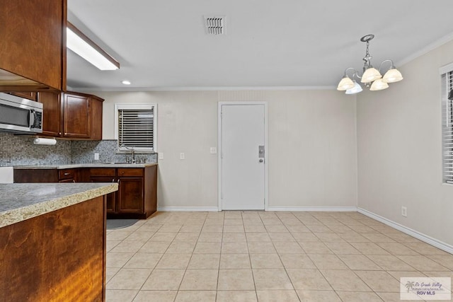 kitchen with light tile patterned floors, light countertops, crown molding, stainless steel microwave, and tasteful backsplash