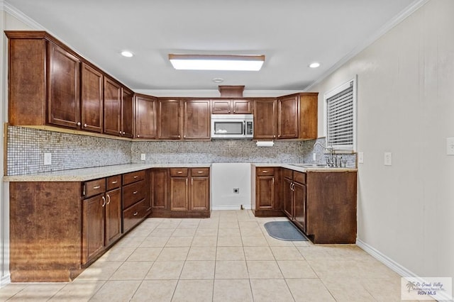 kitchen with light tile patterned flooring, ornamental molding, a sink, stainless steel microwave, and tasteful backsplash