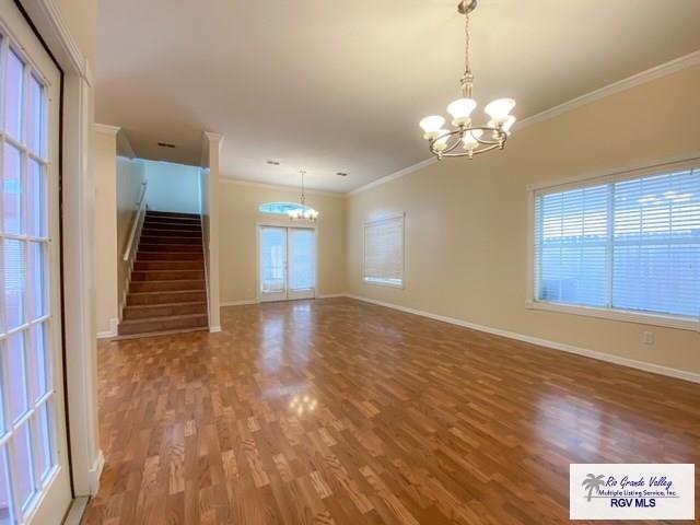 144 Country Club Rd Unit 1, Brownsville, TX 78520 - empty room featuring baseboards, a notable chandelier, ornamental molding, stairway, and wood finished floors