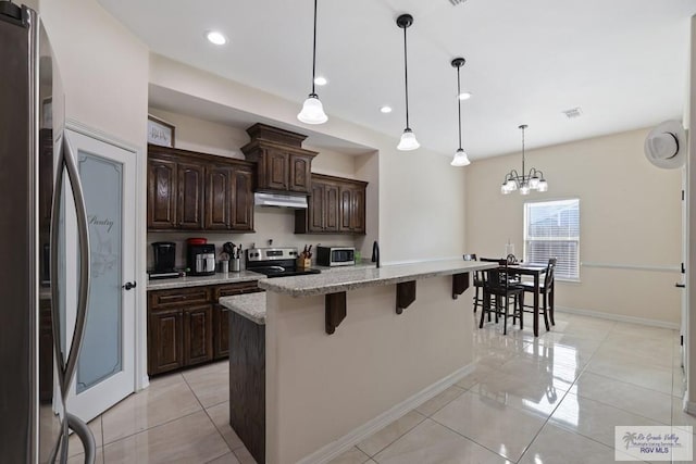 kitchen with light stone countertops, stainless steel appliances, under cabinet range hood, a kitchen bar, and dark brown cabinetry