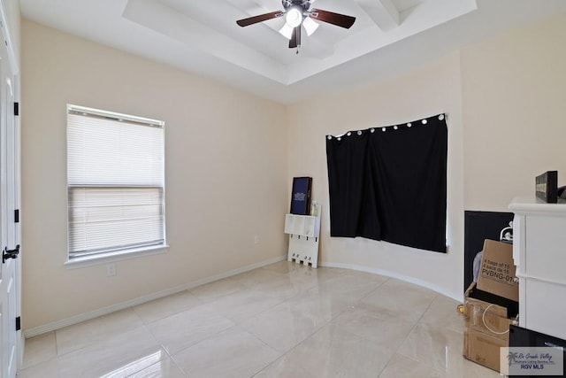 empty room with baseboards, ceiling fan, and a tray ceiling