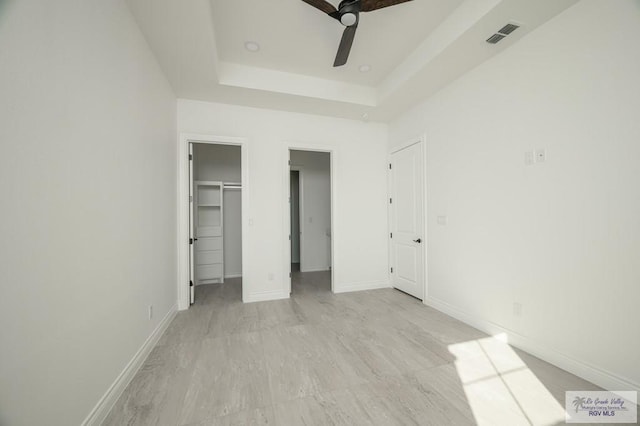 unfurnished bedroom featuring ceiling fan, a raised ceiling, a spacious closet, and a closet