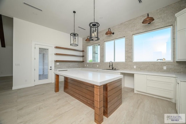 kitchen with backsplash, decorative light fixtures, white cabinetry, and sink