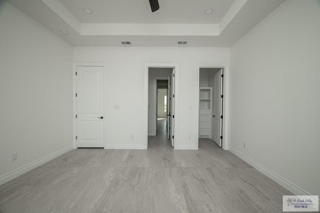 unfurnished bedroom with light wood-type flooring, a raised ceiling, and ceiling fan