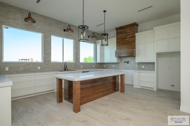 kitchen with sink, hanging light fixtures, a kitchen island, decorative backsplash, and white cabinets