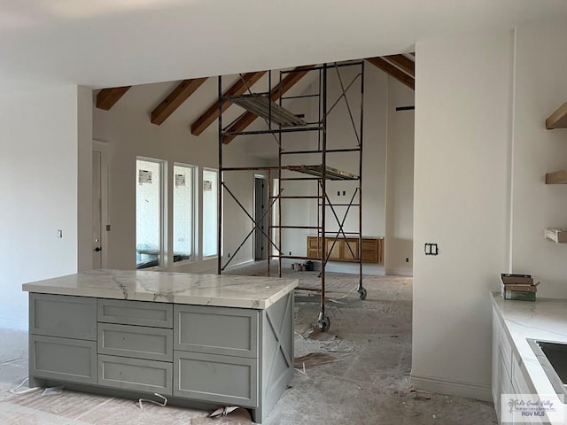 kitchen featuring gray cabinets, light stone counters, and vaulted ceiling with beams