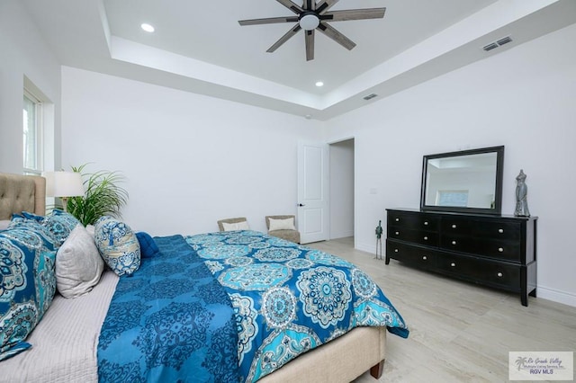 bedroom with a raised ceiling, ceiling fan, and light hardwood / wood-style flooring