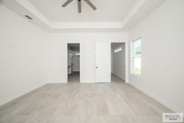 unfurnished bedroom featuring a raised ceiling, ceiling fan, and light hardwood / wood-style floors