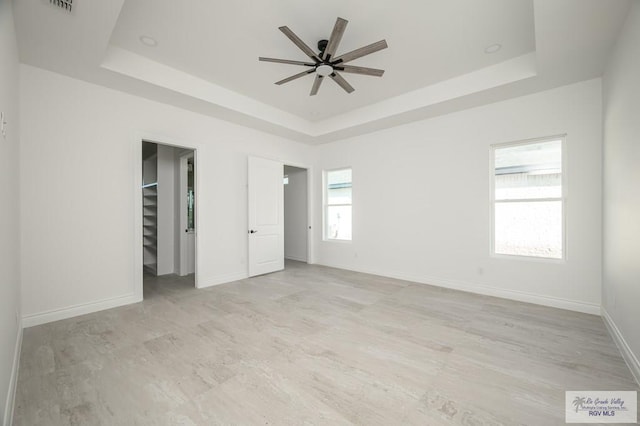 unfurnished bedroom featuring a tray ceiling, a walk in closet, ceiling fan, and a closet