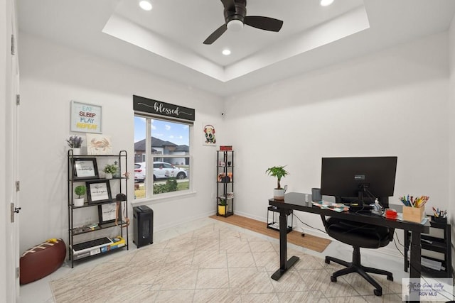 office area with a raised ceiling, ceiling fan, and light wood-type flooring