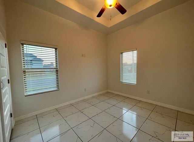 unfurnished room with a tray ceiling, a wealth of natural light, and ceiling fan