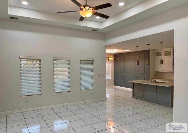 kitchen featuring ceiling fan, sink, a high ceiling, a raised ceiling, and decorative light fixtures