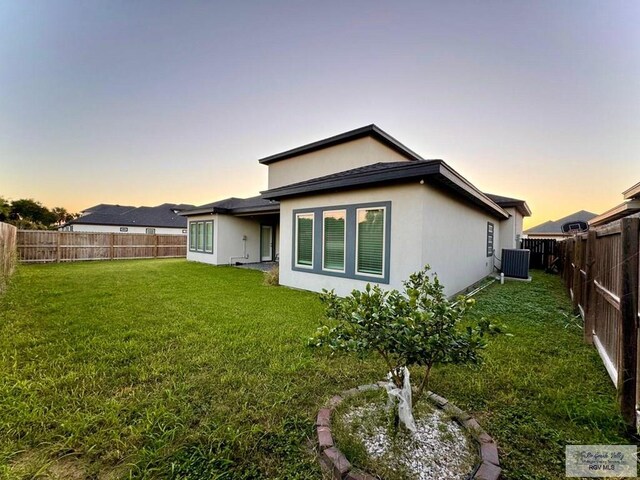 back house at dusk with a yard and central AC unit