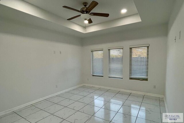 spare room with ceiling fan and a raised ceiling