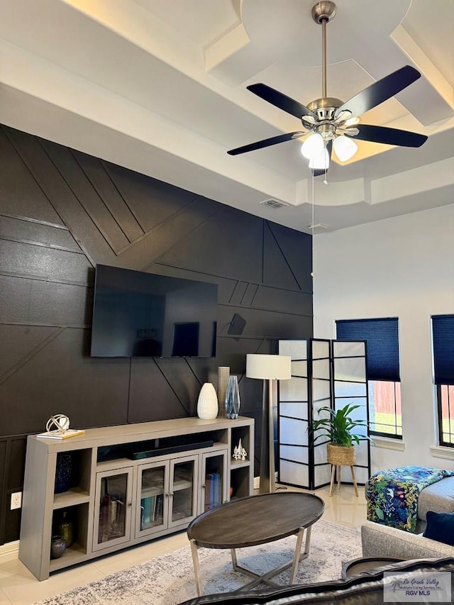 living room with tile patterned flooring, ceiling fan, wooden walls, and a tray ceiling