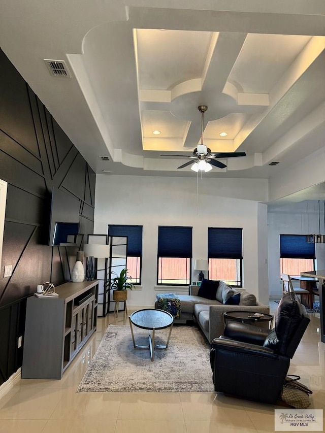 tiled living room with coffered ceiling, a tray ceiling, ceiling fan, and a high ceiling