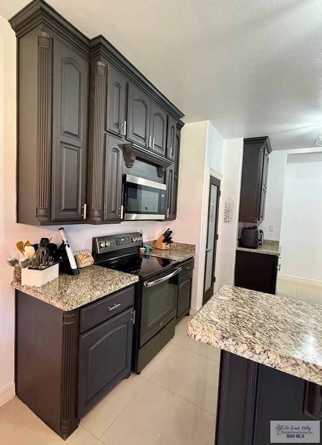 kitchen with light tile patterned floors, baseboards, stainless steel microwave, light stone counters, and black electric range