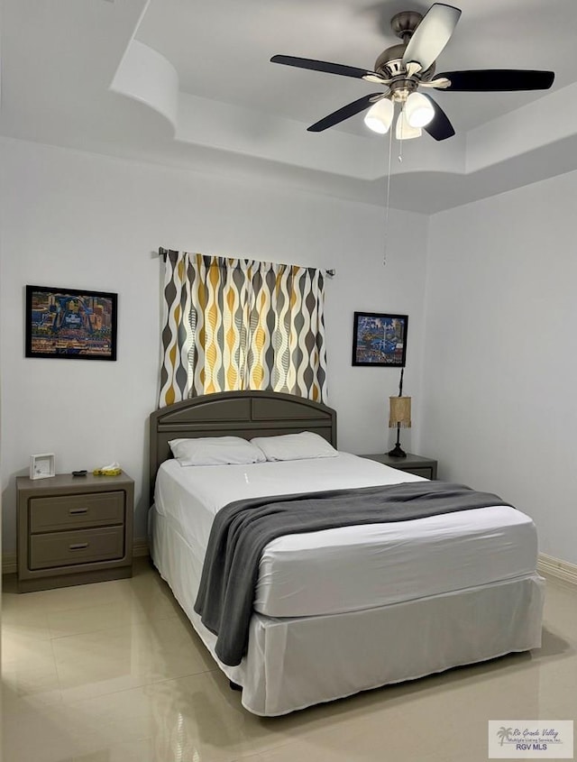 bedroom featuring light tile patterned floors, ceiling fan, a tray ceiling, and baseboards