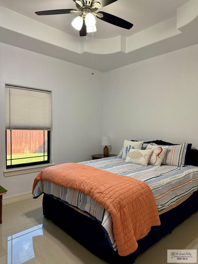 bedroom with a tray ceiling, light tile patterned flooring, a ceiling fan, and baseboards