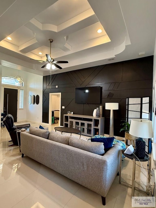 tiled living room featuring a tray ceiling, ceiling fan, and wood walls