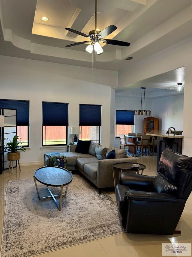 tiled living room with a raised ceiling, ceiling fan, and a high ceiling