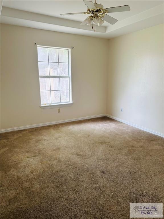 carpeted spare room featuring a raised ceiling and ceiling fan