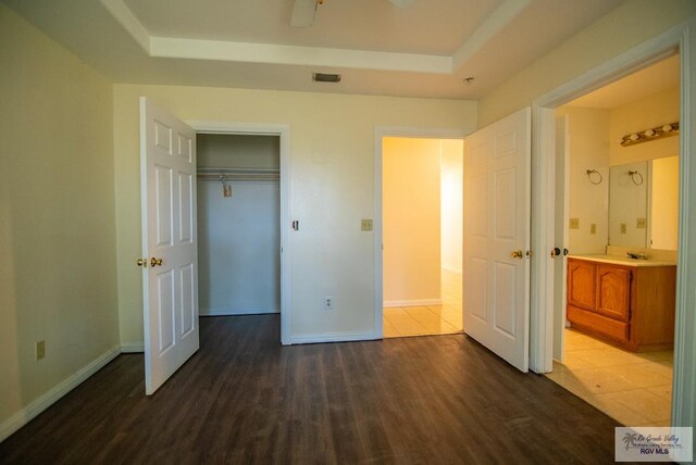 3630 Sun Dr, Harlingen, TX 78552 - unfurnished bedroom featuring a tray ceiling, dark wood-style floors, baseboards, and ensuite bathroom