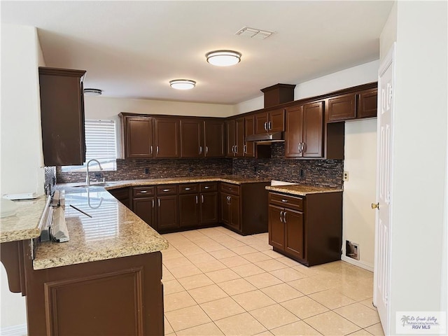 kitchen featuring light stone countertops, dark brown cabinetry, light tile patterned flooring, and sink