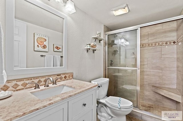 bathroom featuring vanity, toilet, a shower with door, and tasteful backsplash