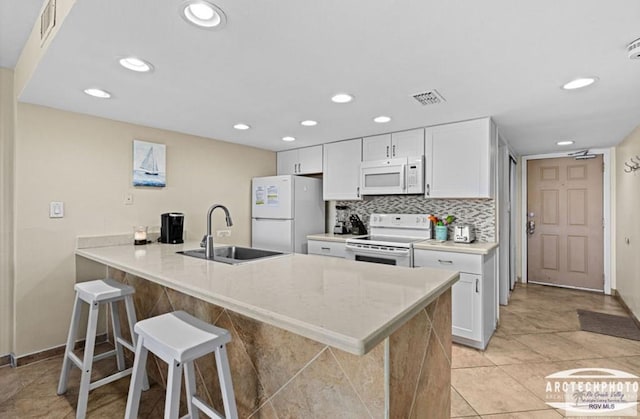 kitchen with kitchen peninsula, a kitchen breakfast bar, white appliances, sink, and white cabinetry