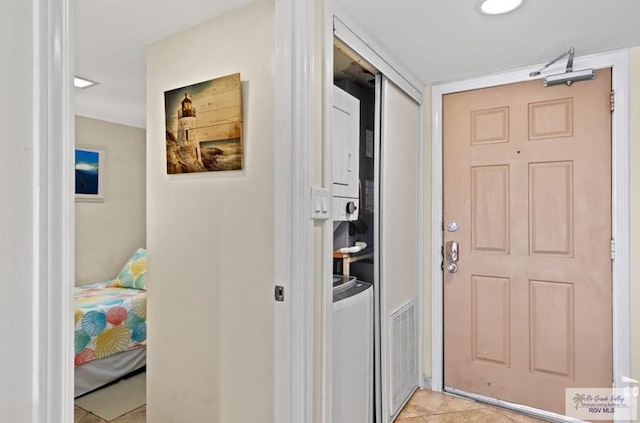 hall with light tile patterned floors and stacked washing maching and dryer