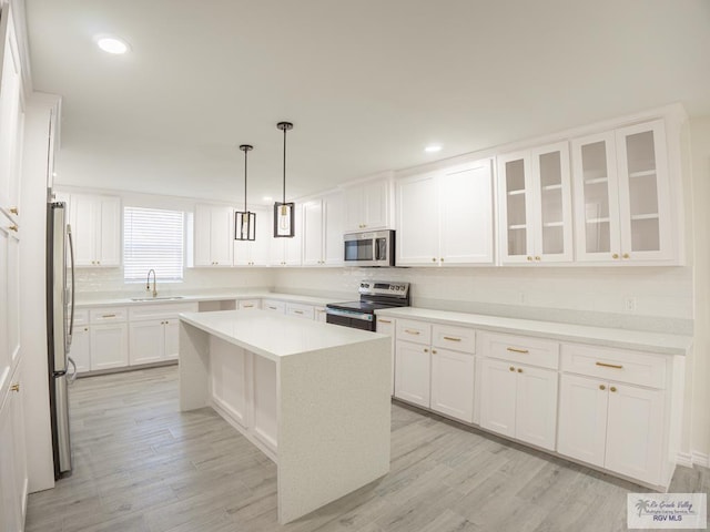 kitchen featuring sink, white cabinetry, stainless steel appliances, a kitchen island, and decorative light fixtures