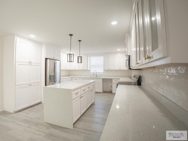 kitchen with sink, hanging light fixtures, appliances with stainless steel finishes, a kitchen island, and white cabinets