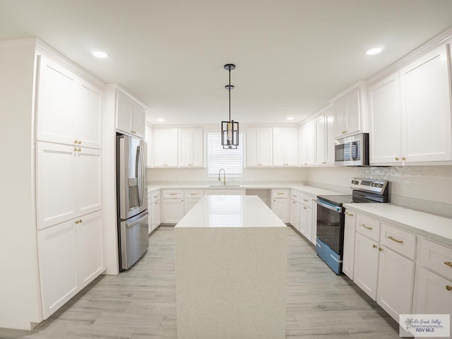 kitchen with sink, appliances with stainless steel finishes, a center island, white cabinets, and decorative light fixtures