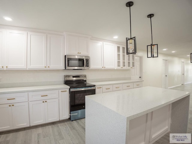 kitchen featuring a kitchen island, decorative light fixtures, white cabinetry, light hardwood / wood-style floors, and stainless steel appliances