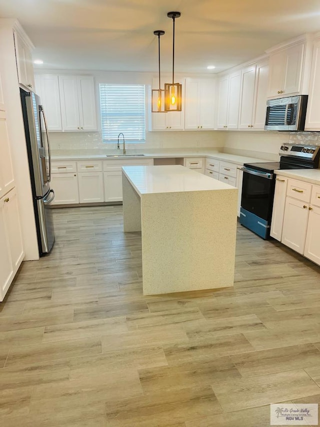 kitchen with a kitchen island, decorative light fixtures, white cabinetry, sink, and stainless steel appliances