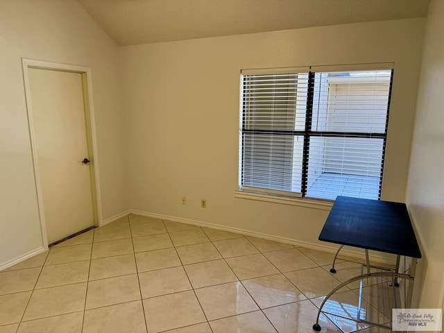 unfurnished room featuring light tile patterned floors, vaulted ceiling, a wealth of natural light, and baseboards