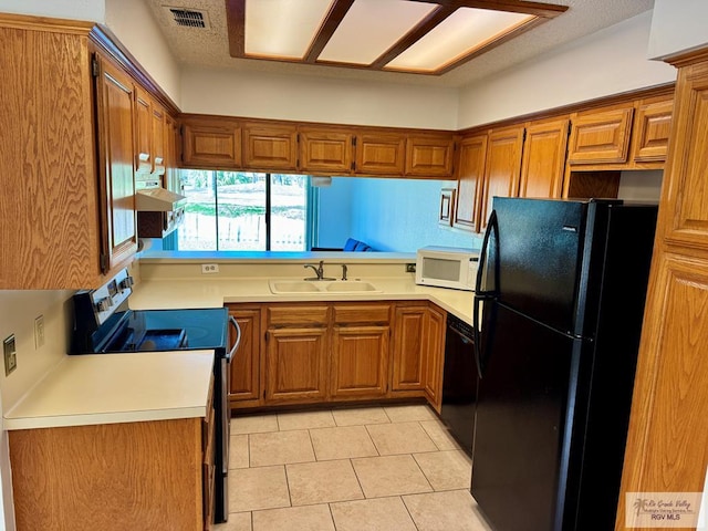 kitchen with visible vents, brown cabinetry, light countertops, black appliances, and a sink