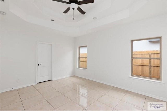 tiled spare room with ceiling fan and a tray ceiling