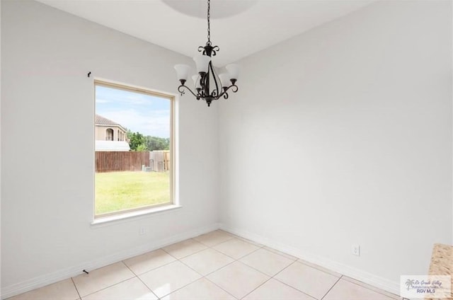 empty room with light tile patterned floors, a healthy amount of sunlight, and an inviting chandelier